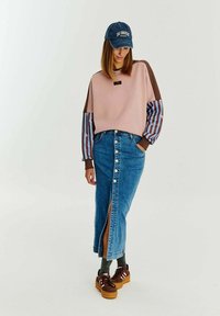 Svetlo ružová mikina s hnedými a pruhovanými rukávmi, skombinovaná s modrou džínsovou sukňou s predným rozparkom a detailom gombíka, hnedé tenisky.