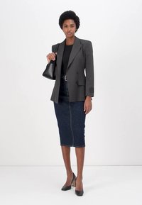 Blazer noir à rayures sur un haut noir, associé à une jupe crayon en denim foncé. Les accessoires comprennent un sac à main noir et des talons noirs.