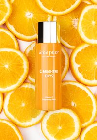 Vitamin C oplysende tonicflaske med en blank sølvhætte, cylindrisk form og en livlig orange farve, omgivet af appelsinskiver.