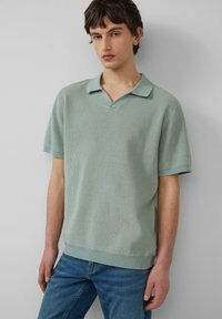 Polo en tricot vert clair avec un col en V, des manches courtes et des poignets côtelés. Associé à un jean bleu délavé.