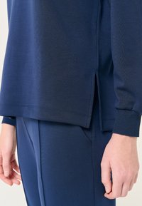 Top sportivo blu navy con texture a coste, spacchi laterali e polsini aderenti. Abbinato a pantaloni blu navy coordinati, che mettono in risalto un design senza cuciture.