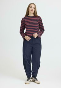 Röd och marinrandig långärmad skjorta som kombineras med marinblå byxor med sidoknäppning och dragsko i midjan. Sneakers fulländar outfiten.