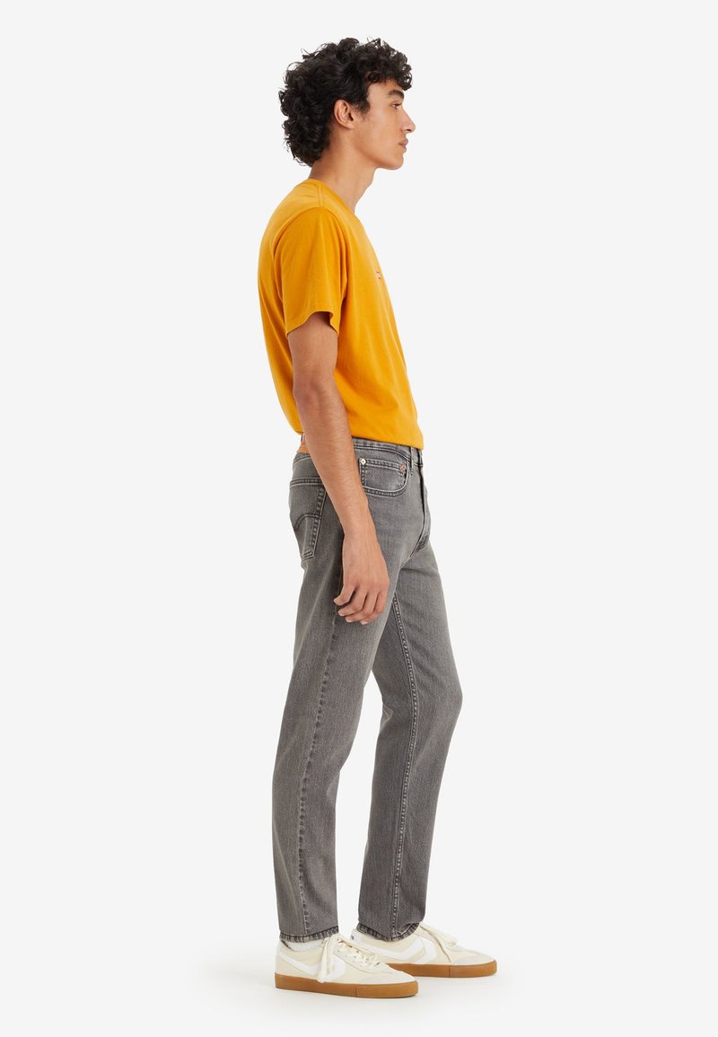 Jeans grises de corte recto, combinados con una camiseta amarilla brillante. El modelo lleva zapatillas de deporte off-white con suelas de goma marrón.