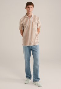 Camisa de manga corta, con cuello y rayas estrechas en marrón y blanco, que cuenta con un bolsillo en el pecho, combinada con vaqueros de color azul claro y zapatillas color menta.