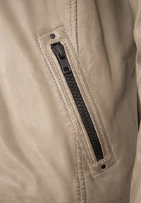 Beige Lederjacke mit strukturierter Oberfläche, ausgestattet mit einem schwarzen Reißverschluss auf der linken Seite und einem gesteppten Nahtdetail.