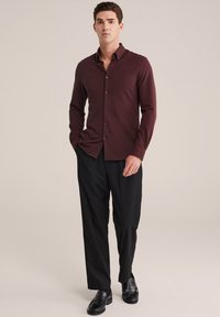 Burgundijas krāsa ilgi piedurkņu pogājamā krekla ar slim fit, ar apkakli un tumšām pogām, kopā ar melniem biksēm un spīdīgām melnām kurpēm.