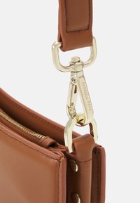 Borsa a tracolla in pelle marrone con un attacco in metallo dorato, apertura con zipper e cuciture decorative lungo i bordi.