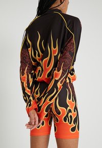 Černý outfit s oranžovými grafikami plamenů, skládající se z dlouhého rukávu a odpovídajících šortek. Hladká textura s podrobnými vzory na látce.