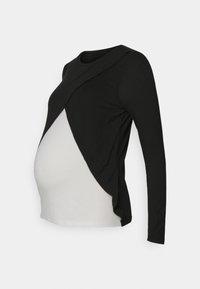 Top premaman a maniche lunghe in bianco e nero con un design asimmetrico, caratterizzato da un sovrapposizione nera e una sezione inferiore bianca, realizzato in tessuto elasticizzato.