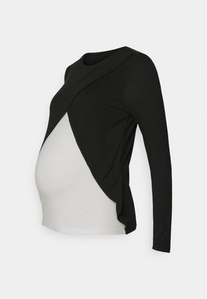 Haut de maternité à manches longues en noir et blanc avec un design asymétrique, présentant un superposé noir et une partie inférieure blanche, fabriqué en tissu extensible.