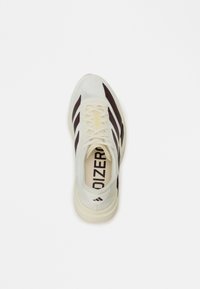 Weißer Sportschuh mit dunkelbraunen Streifen und strukturiertem Gewebe. Verfügt über einen gepolsterten Schaft und eine dicke Sohle. Branding im Inneren sichtbar.