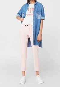 Vestido de camisa de mezclilla, manga corta, azul claro, con dos bolsillos en el pecho; camiseta blanca con estampado rojo, pantalones rosa claro y zapatillas blancas.