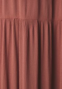Robe couleur rouille avec un tissu texturé et froissé. Présente des plis froncés, accentuant le volume et le mouvement. Finition lisse, matériau léger.
