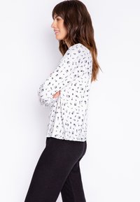 Långärmad vit topp med svart blommönster, lätt tyg, rund hals, och avslappnad passform, matchad med svarta ribbade byxor.