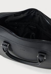 Fekete bőrből készült kézitáska mintás fogantyúkkal, nyitott cipzár, amely tágas belső teret mutat cipzáras zsebbel és márkás béléssel.