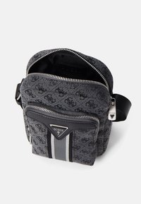 Bolso de hombro de lienzo gris oscuro con un patrón texturizado, bolsillo frontal con cremallera, acentos de cuero negro y herrajes plateados. Presenta un detalle a rayas.