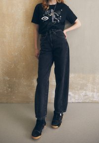 Black graphic t-shirt features a basketball design, paired with high-waisted black jeans and black sneakers with a textured sole.