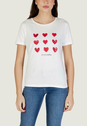 Donna che indossa una maglietta bianca con nove cuori rossi disposti in tre file e il testo "amore sopra ogni cosa" sotto i cuori.