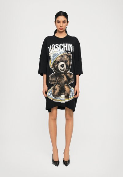 Robe surdimensionnée noire avec un graphique d'ours portant un chapeau décoratif, au centre. Manches courtes et design à ourlet droit.