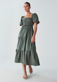 Zelena maksimalna haljina od pamuka sa kvadratnim dekolteom, kratkim napuhanim rukavima, složenim dizajnom i elastifikovanim gornjim delom. Jednostavna, lepršava silueta.