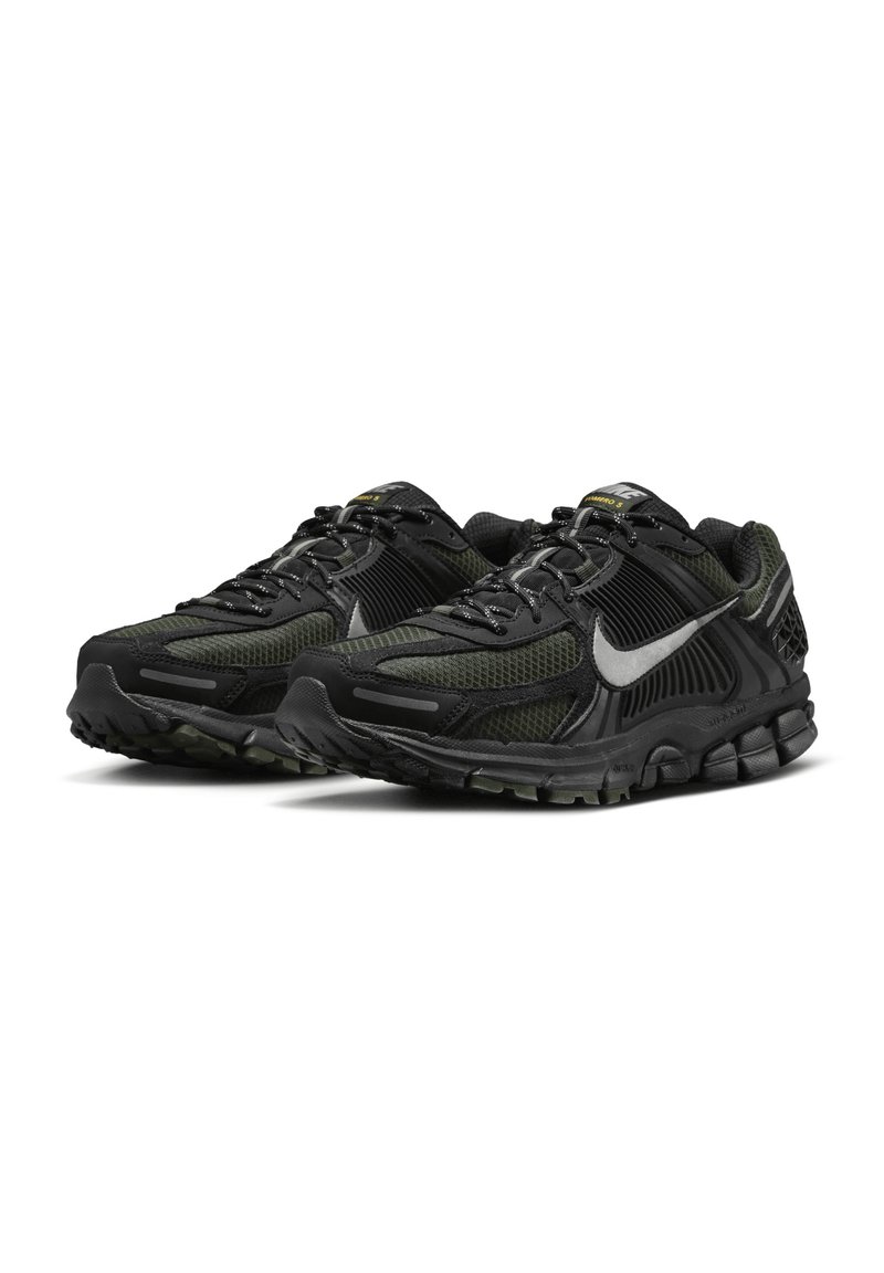 Chaussures de sport noires et vertes avec une tige en mesh, des détails texturés, un embout renforcé et une semelle en caoutchouc avec des motifs de traction visibles.