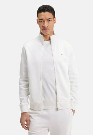 Sweatshirt zippé blanc avec col montant, poignets et ourlet côtelés, fabriqué en tissu doux avec un discret logo sur la poitrine.