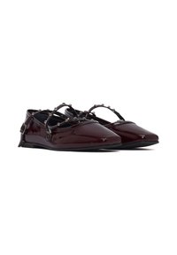 Des ballerines en cuir verni bordeaux avec un bout pointu, des brides croisées ornées de perles métalliques décoratives, et une semelle noire plate.