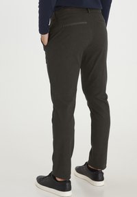 Slim-fit, mørkegrå bukser med en tekstureret stof, har en lynlåslomme bagpå og er parret med sorte sneakers.