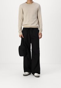 Beżowy sweter dzianinowy, luźne czarne spodnie i mała czarna torebka na ramię. Sneakersy z szarymi akcentami. Prosta, casualowa stylizacja.