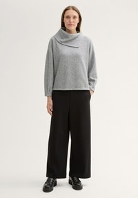 Grau, Langarm-Oberteil mit Stehkragen, kombiniert mit weiten schwarzen Hosen und schwarzen Plateauschuhen. Texturiertes, lässiges Design.