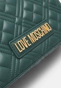 Quiltowana zielona torba z faux skóry z złotym logo "LOVE MOSCHINO". Projekt jest płaski z teksturowaną powierzchnią i starannym szyciem.