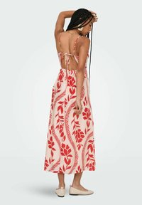 Robe maxi en tissu pêche clair avec des motifs floraux rouges. Bretelles spaghetti, dos ouvert avec liens et jupe fluide.