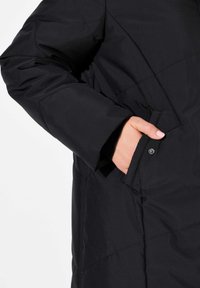 Svart vadderat jacka med hög krage, med en sidoficka och mjuk textur. Designen inkluderar quiltad sömnad för extra detalj.