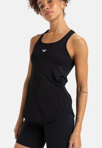 Musta urheilu-toppi, joka on valmistettu sileästä, joustavasta kankaasta. Siinä on pyöreä pääntie, ohuet olkaimet ja pieni logo rinnassa.