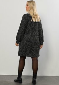 Abito nero con una stampa leopardata testurizzata, maniche lunghe e una vestibilità rilassata, abbinato a stivaletti neri e collant neri trasparenti.