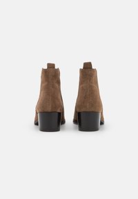 Botas de tobillo de ante marrón con tacón de bloque, que cuentan con un diseño minimalista y lengüetas en la parte superior para facilitar su uso.