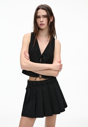 Zwarte cropped top met een diepe V-hals en trekkoordsluiting, gecombineerd met een zwarte plissé mini-rok met een elastische tailleband.