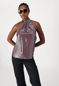 Top halter de color malva metálico con tejido texturizado y cuellos fruncidos, combinado con pantalones de mezclilla oscuros y gafas de sol.