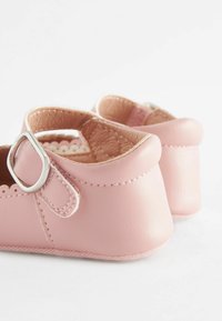 Pink leather shoes with scalloped edges and a side buckle detail. Rounded back and soft texture, designed for comfort.