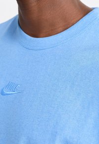 Ljusblå bomulls t-shirt med rund halsringning, prydd med en broderad Nike-logotyp i en något mörkare nyans. Mjuk och slät textur.