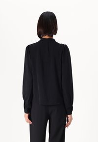 Black blouse with long, puffed sleeves, a rounded collar, and a loose fit, made of lightweight fabric, featuring a plain texture.