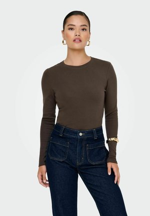 Maglietta a maniche lunghe marrone in tessuto liscio, abbinata a jeans in denim blu scuro a vita alta con tasche evidenti e dettagli di cucitura.
