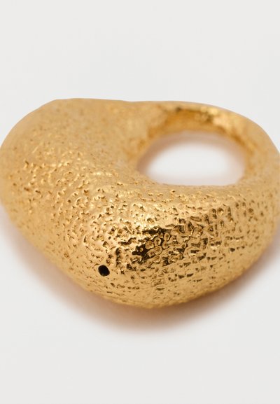 Zeltīta gredzena ar teksturētu, neregulāru virsmu un apaļu atvērumu, demonstrējot metāliski spīdumu un unikālus dizaina elementus.