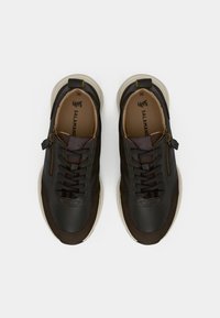 Tumedast pruunist nahast tenne situ, ümarate varvastega, paeltega ees, külgselt lukuga, beežil tallal ning reljeefsete detailidega. Suurus 36 on sees märgitud.