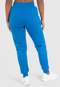 Helle blaue Jogginghose mit geripptem Taillenbund und Bündchen, mit glatter Textur. Kombiniert mit weißen Sportschuhen.