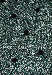 Tissu texturé vert foncé, blanc et noir avec des boutons ronds noirs disposés en rangées.