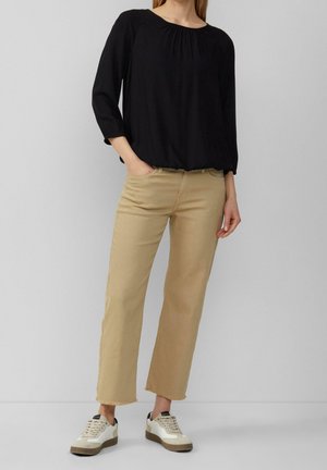 Camisa negra de manga larga con escote fruncido, combinada con jeans rectos beiges y zapatillas blancas con acentos marrones y cordones.