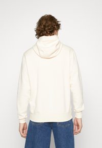 Krämfärgad hoodie av mjukt tyg, med stor huva, ribbade muddar och en avslappnad passform med minimala designdetaljer.