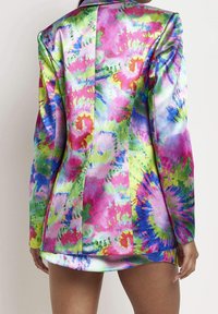 Mujer llevando un blazer de tie-dye vibrante en tonos de rosa, verde, azul y amarillo, visto desde atrás por encima de su muslo.