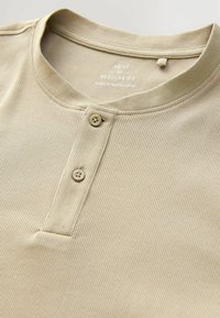 Camisa henley de color beige con un cuello redondo, placket de dos botones y textura suave. La etiqueta muestra "NEXT" y "REGULAR FIT."